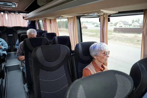 Envejecida mujer caucásica con el pelo gris sentado por la ventana dentro del autobús —  Fotos de Stock