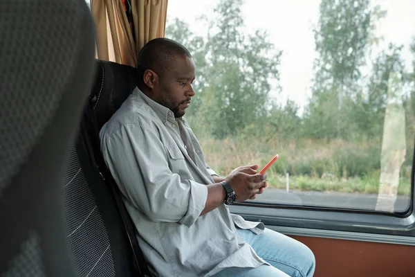 Oldalnézet a fiatal afrikai férfi okostelefon ül az ablakban — Stock Fotó