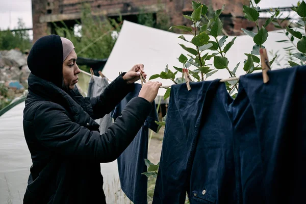 Giovane migrante donna appeso vestiti puliti sulla corda — Foto Stock