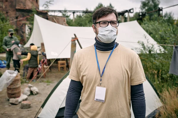 Молодой волонтер в защитной маске стоит в лагере беженцев — стоковое фото