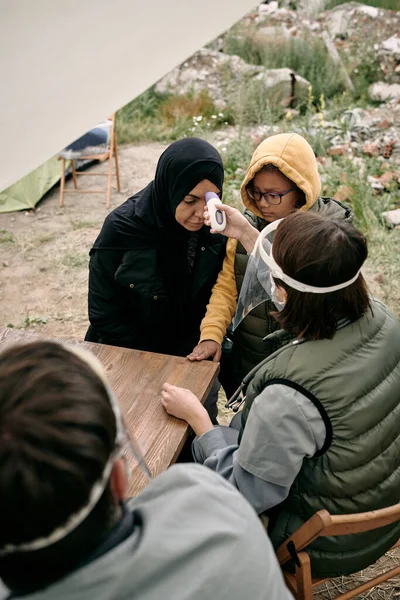 Врач-доброволец измеряет температуру тела молодой женщины-беженки — стоковое фото