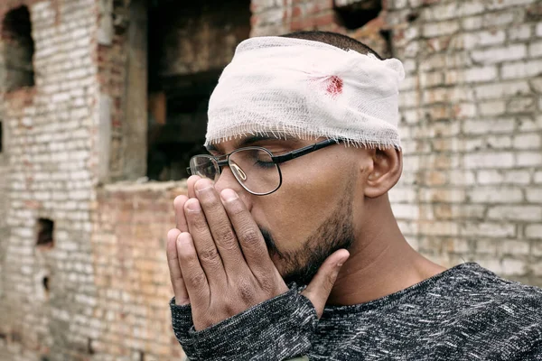Joven herido con vendaje alrededor de la cabeza manteniendo las manos juntas cerca de su cara — Foto de Stock
