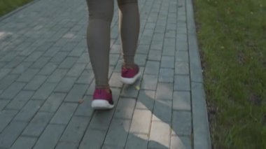 Güneşli bir günde parkta tek başına koşan dar spor giysili, geniş beden Afro-Amerikan bir kadının dikiz aynasından yavaş çekimleri.