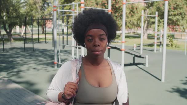 在阳光灿烂的日子里 年轻而活跃的非洲裔美国女子站在室外运动场上的运动器材旁边拍照时的中特写 — 图库视频影像