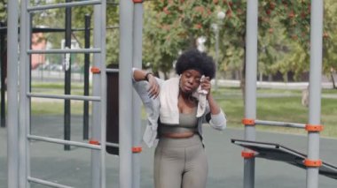 Sıkı spor giyimli, yorgun ve iri yarı Afro-Amerikan bir kadının vücut çalışmasından sonra yüzündeki teri beyaz havluyla silişi.