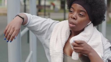 Açık havada idman yaptıktan sonra terini havluyla silen yorgun Afro-Amerikan kadının orta boy yakın çekimi.