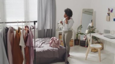 Aktif giyimli, kulaklık takan, spor çantalı ve spor yapmak için evden çıkan Afro-Amerikan kadının yavaş çekimleri.