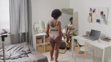 Dikiz aynasından, yatak odasında aynanın önünde dikiz aynasındaki kıvrımlı Afro-Amerikan kadının belini mezurayla ölçerken yavaş çekilen görüntüsü.