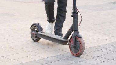 Düşük seviyeli yavaş çekim. Beyaz spor ayakkabılı, tanınmayan erkek bacakları e-scooter 'da dikiliyor ve açık havada sürüşe başlıyor.