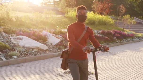 在阳光明媚的日子里 身穿红色毛衣 头戴面罩 头戴电动车 站在城市公园里的非洲裔美国商人的中等速度慢画像 — 图库视频影像
