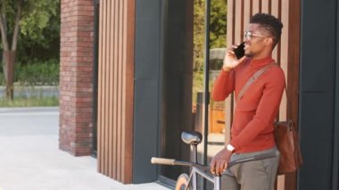 Güneşli bir günde şehrin göbeğinde telefonla konuşan şık giysili ve gözlüklü yakışıklı Afro-Amerikan delikanlının orta yavaş çekimi.