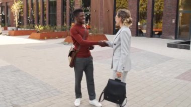 Şehir merkezinde, şık giyimli, neşeli, çoklu etnik iş çifti şehir merkezinde buluşup el sıkışarak birbirlerini selamlarken orta yavaş çekimler.