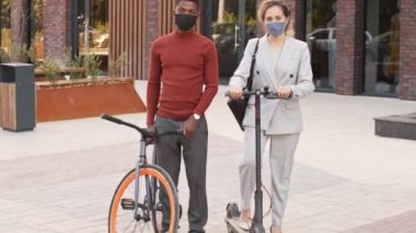 Bisiklet ve elektrikli scooterlı, şık günlük kıyafet giyen ve iş bölgesinde kameraya poz veren genç ve çok ırklı iş kadınlarının yavaş yavaş portresi.