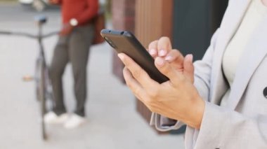 Akıllı günlük kıyafet giyen tanınmayan iş kadınının yavaş yavaş yakın çekimi açık havada duran akıllı telefondan mesaj iletiyor.
