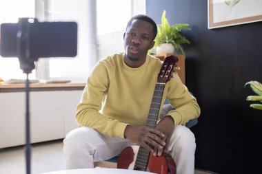 Akıllı telefon kamerasının önünde gitar çalan kendine güvenen genç bir müzik koçu.