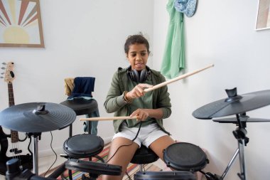 Çift ırklı liseli kız ahşap bagetlerle davul çanlarını çalıyor.