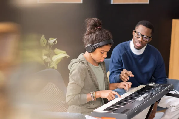 Cute schoolgirl pushing keys of piano keyboard during home lesson — Stock Photo, Image