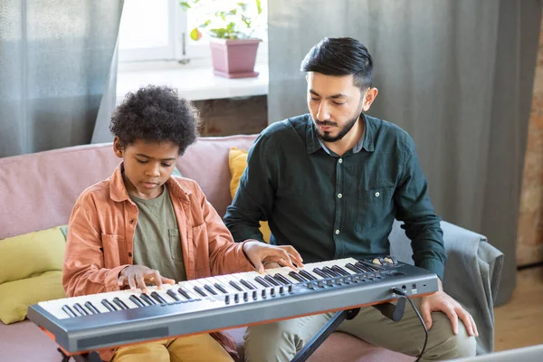 Cute schoolboy pressing keys of piano keyboard with his teacher near by — Stock Photo, Image