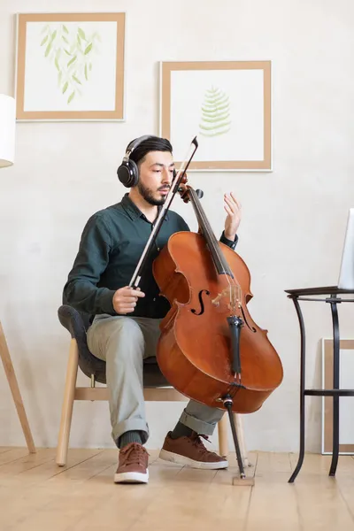 Jovem professor de música com violoncelo sentado na sala doméstica — Fotografia de Stock