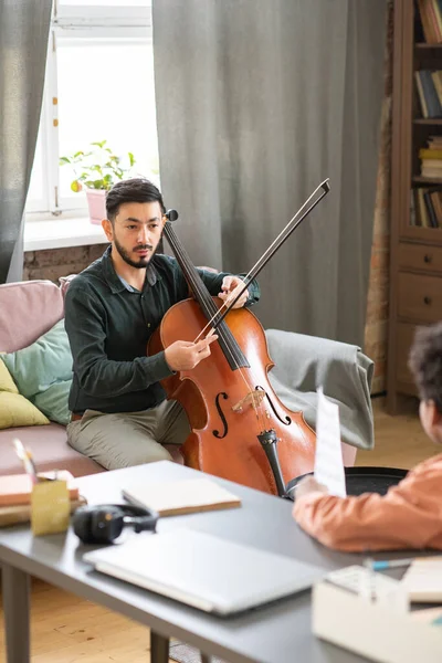 Jovem professor de música confiante explicando estudante como jogar violoncelo — Fotografia de Stock