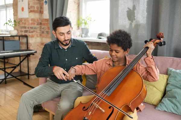 Cute biracial boy playing cello while sitting next to his teacher — Stock Photo, Image