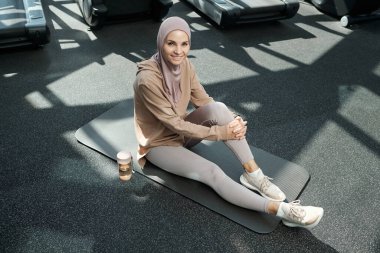 Spor salonundaki paspasın üzerinde oturan mutlu genç bayan.