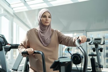 Spor malzemelerinin başında duran tesettürlü genç bayan.