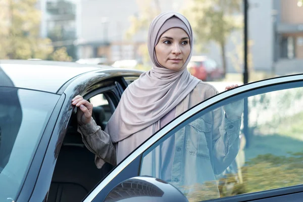 Jonge vrouw in hijab staan door de deur van de auto terwijl het krijgen van uit het — Stockfoto