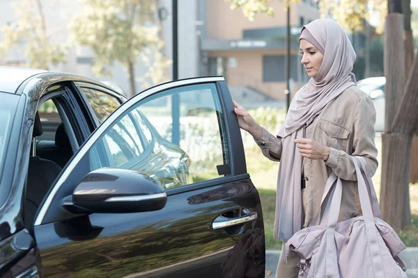 Joven mujer musulmana contemporánea con bolsa rosa va a cerrar la puerta del coche —  Fotos de Stock