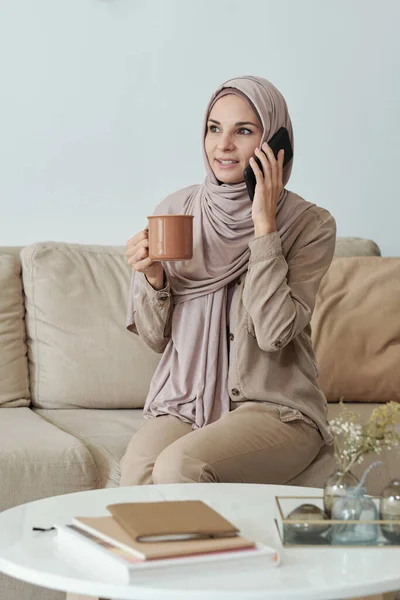 Jonge vrouw in hijab thee drinken en spreken op mobiele telefoon — Stockfoto