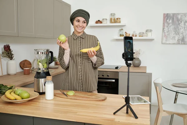 Mladá usmívající se žena ukazuje čerstvé banány a jablka pro své online publikum — Stock fotografie