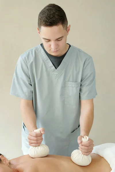Młody masażysta nakładający na plecy woreczki aromatyczne — Zdjęcie stockowe