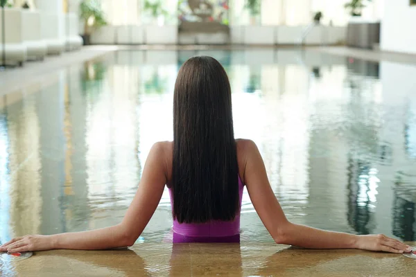 Bakifrån av ung brunett med långt tjockt hår avkopplande i poolen — Stockfoto