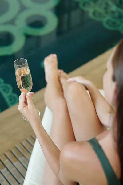 Havuz kenarında otururken elinde şampanya flütü tutan genç bir kadın. — Stok fotoğraf