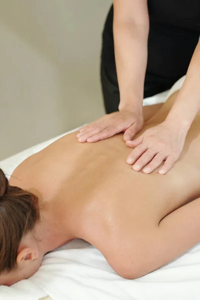Mani di massaggiatore toccando indietro di giovane donna — Foto Stock