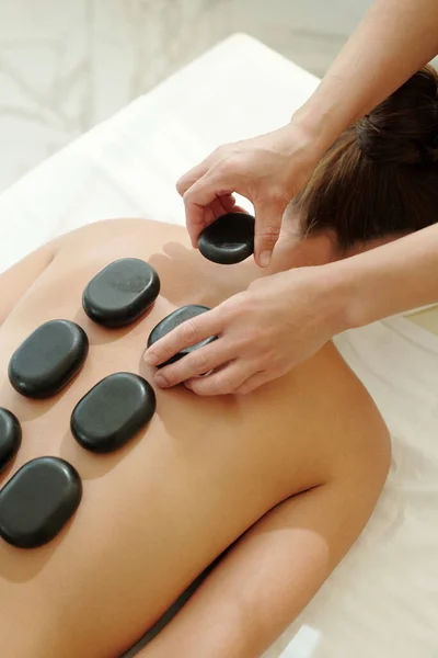 Handen van masseuse zetten hete spa stenen op vrouwelijke rug — Stockfoto