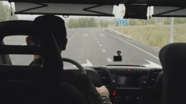Yetişkin bir adamın gündüz vakti boş bir yolda yolcu otobüsü sürüşünün dikiz görüntüsü.