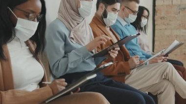 Çeşitli yüz maskeli kadın ve erkek gruplarının iş görüşmelerini beklerken sıraya dizilip başvuru formlarını doldurmalarını bekle.
