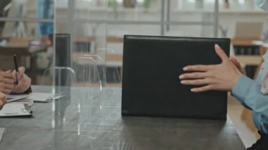 Müslüman kadın iş adayının tesettürlü ve yüz maskeli görüntülerinin orta bölüm takibi. Anti-damlacık plastik ekranı ve şarkı söyleyen belgenin arkasında oturuyor. Sonra da onu tanınmayan İK temsilcilerine teslim ediyor.