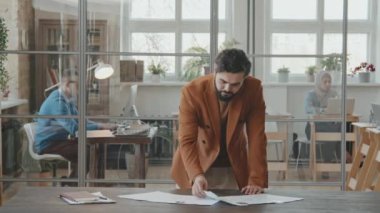 Resmi olarak sakallı erkek İK müdürünün portre fotoğrafı ofiste masanın yanında duruyor ve iş adayı seçerken başvuru formlarına bakıyor, sonra yukarı bakıyor ve kameraya poz veriyor.