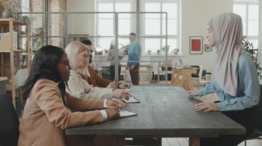 İK temsilcilerinden oluşan bir ekibin açık planlı ofisin konferans masasında oturmasının ve tesettürlü Müslüman bir kadınla iş görüşmesi yapmasının izlenmesi.
