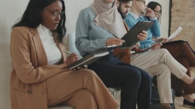 Kafiyeli ve resmi giyinmiş neşeli Müslüman kadını yukarı kaldır. Sandalyeye otur ve Afrikalı-Amerikalı bir kadınla sohbet et. Başvuru formunu doldur ve iş görüşmesi için sırada bekle.