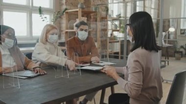 Maskeli Asyalı bir kadının masaya oturup başvuru formunu ofisteki koruyucu ekranın arkasında oturan İK yöneticilerine teslim edişinin izini sürmek. Salgın sırasında iş görüşmesi yapanlar