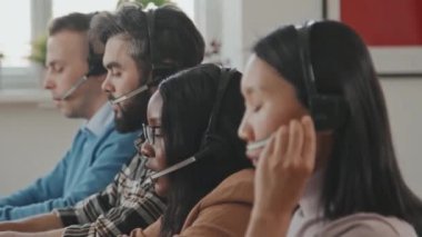 Ofisteki müşterilerle konuşan çağrı merkezi operatörlerinden oluşan farklı bir ekibin yan görüntüsüyle yakından takip ediliyor.