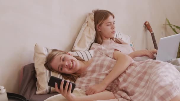 침대에서 휴식을 취하고 전화와 노트북으로 미디어를 둘러보고 쌍둥이 자매들의 — 비디오