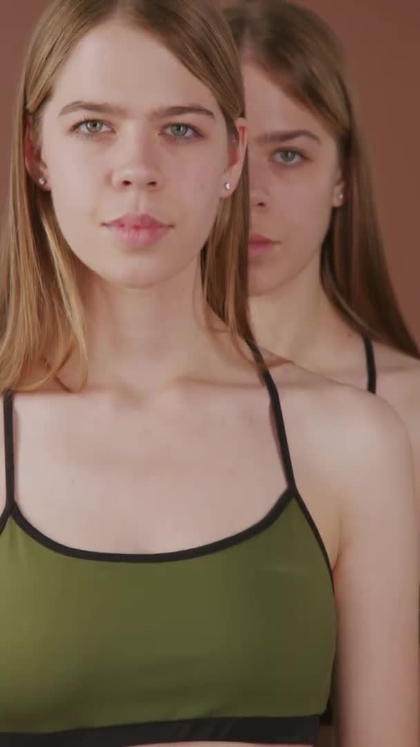 有一对漂亮的孪生姐妹在褐色背景上摆出孤身一人的垂直肖像 — 图库视频影像