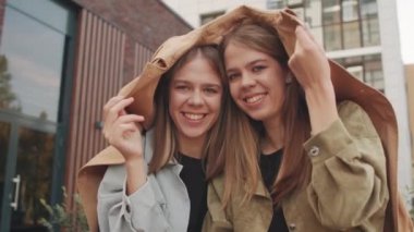 Trençkotun altında saklanan ve dışarıda kameraya gülümseyen ikiz kız kardeşlerin yavaş yavaş portresi.