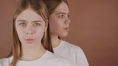 Kahverengi arka planda poz veren genç ikiz kız kardeşlerin yakın plan çekimleri.