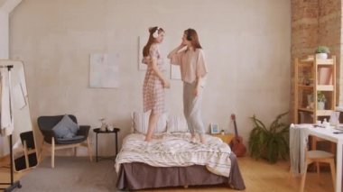 Yatakta dans eden kulaklıklı mutlu ikiz kızların PAN çekimi.