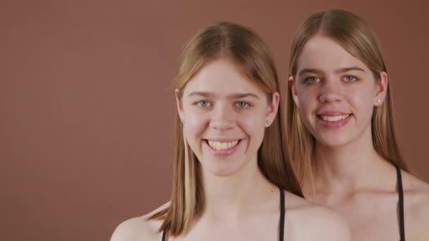 Zdjęcie Portretowe Szczęśliwej Młodej Bliźniaczki Uśmiechniętej Kamery Stojącej Brązowym Tle — Wideo stockowe